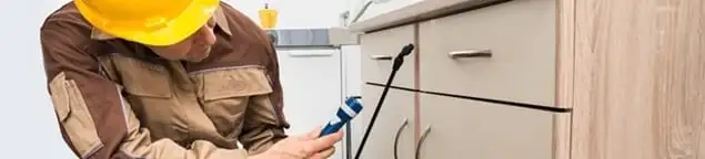 Roach exterminator applying treatment under kitchen cabinets in Aurora, IL
