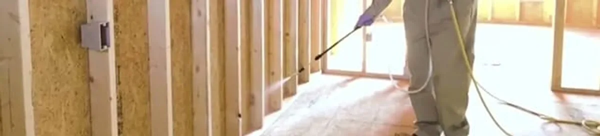 Termite treatment technician applying spray along framing and unfinished walls in Aurora, IL