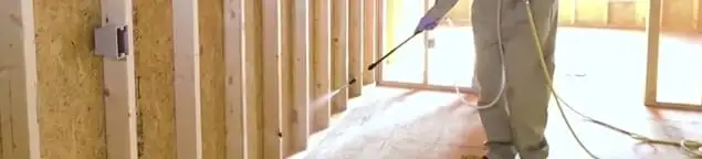 Termite treatment technician applying spray along framing and unfinished walls in Aurora, IL